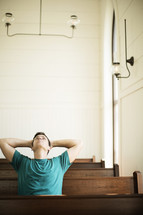 Man looking up and leaning back while praying in a church pew.
