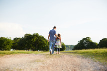 a father and daughter walking down a dirt road talking 