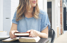 a young woman sitting at an outdoor table with a Bible and journal 
