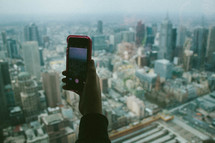 hand holding up a cellphone in front of a cityscape 