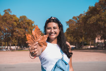 a smiling woman holding a fall leaf 