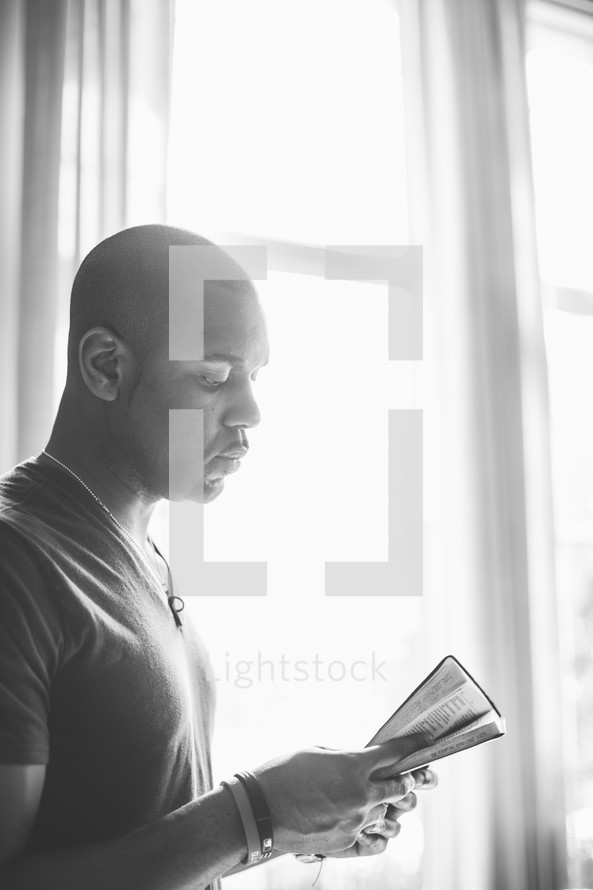 Praying man holding a Bible in front of a window.