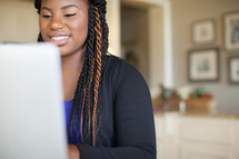 Smiling woman with braids looking at a computer monitor.