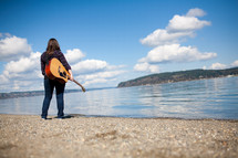 woman holding a guitar standing by a lake