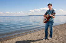 man playing a guitar on the shore of a lake