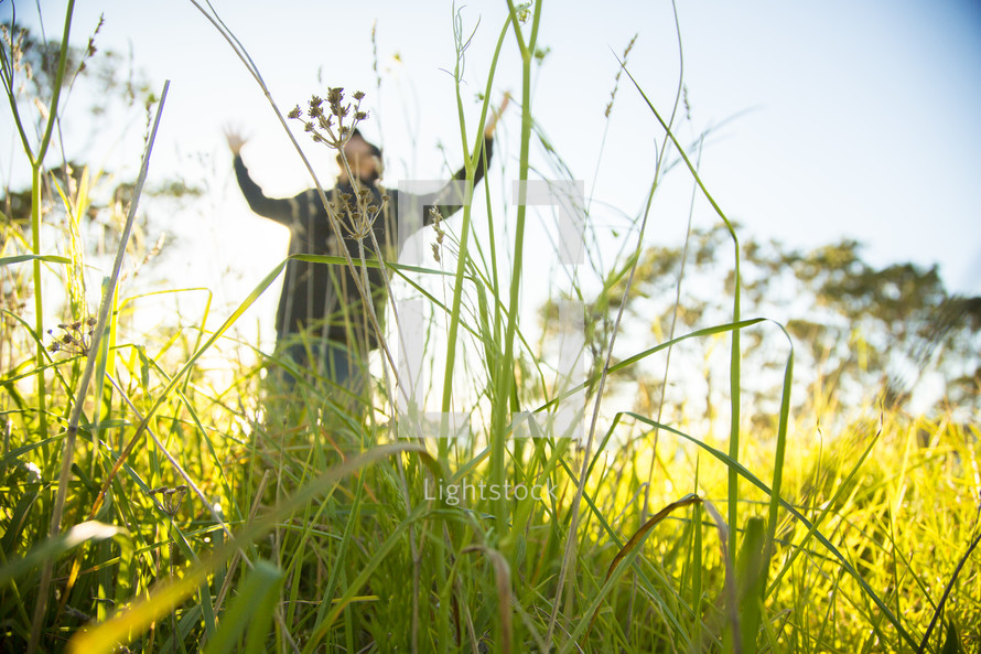 man standing outdoors in tall grass with raised arms 