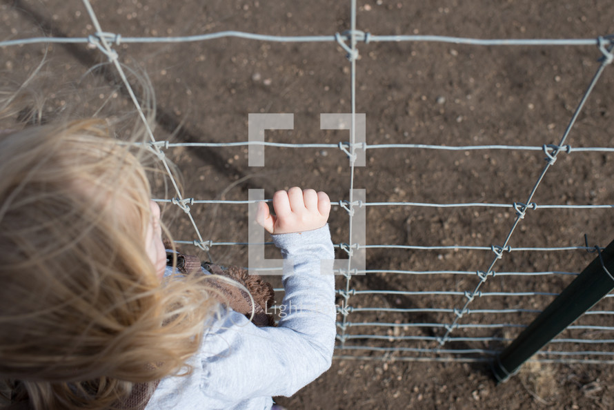 a girl child looking through a wire fence 
