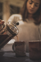 A woman pouring coffee into a mug from a French press