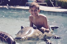 a boy on an alligator pool float in a swimming pool in summer 