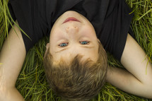 Boy laying in the grass outside.