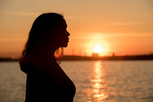silhouette of a woman standing by water at sunset 
