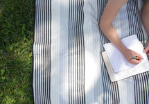a girl lying on a blanket in the grass reading a Bible and writing in a journal 