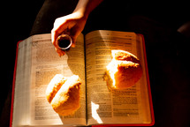 A child holding a communion cup over a Bible with broken bread.