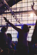 a woman in an audience standing with raised hands praising God 