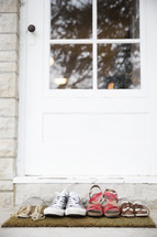 A family's shoes in front of a door on a doormat.