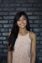 A smiling young woman standing against a gray brick wall.