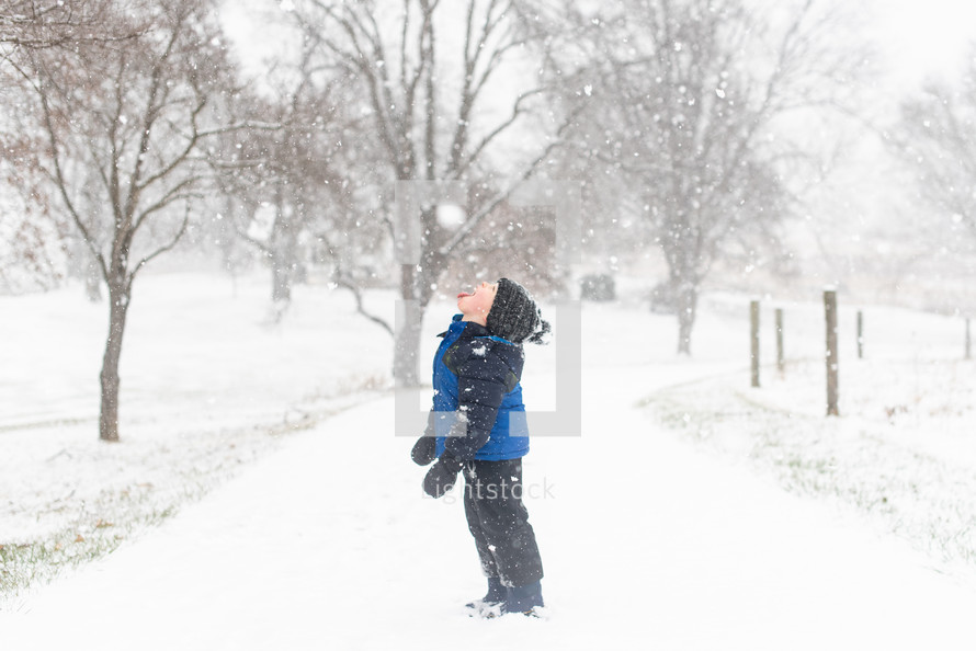 Small child playing in the snow - sticking out tongue to catch snow flakes