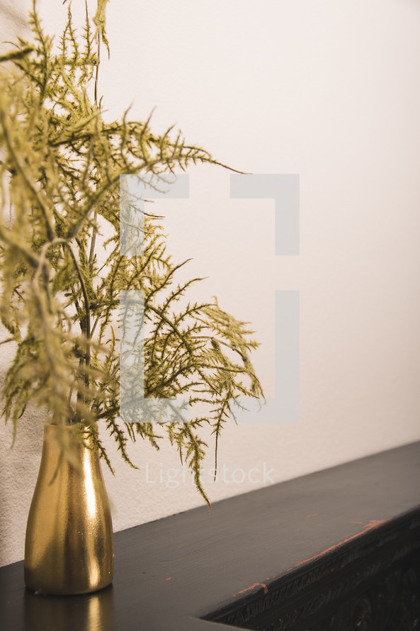 greenery in a gold vase on a mantle 