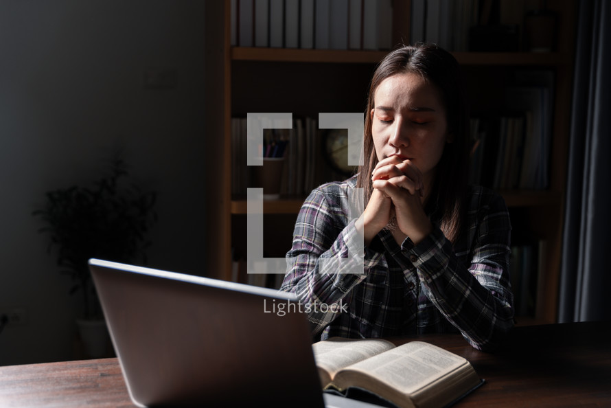 Woman praying with Bible and computer