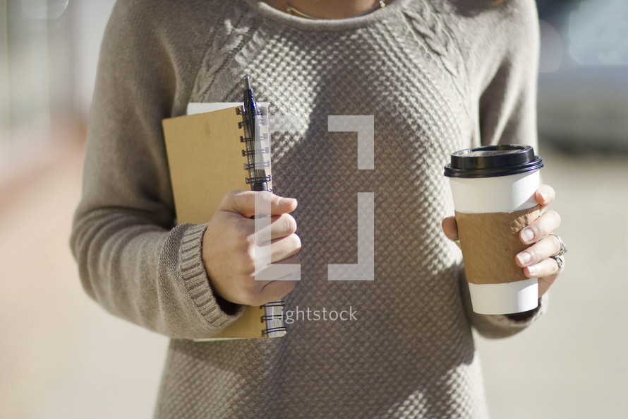 A woman holding a journal and coffee 