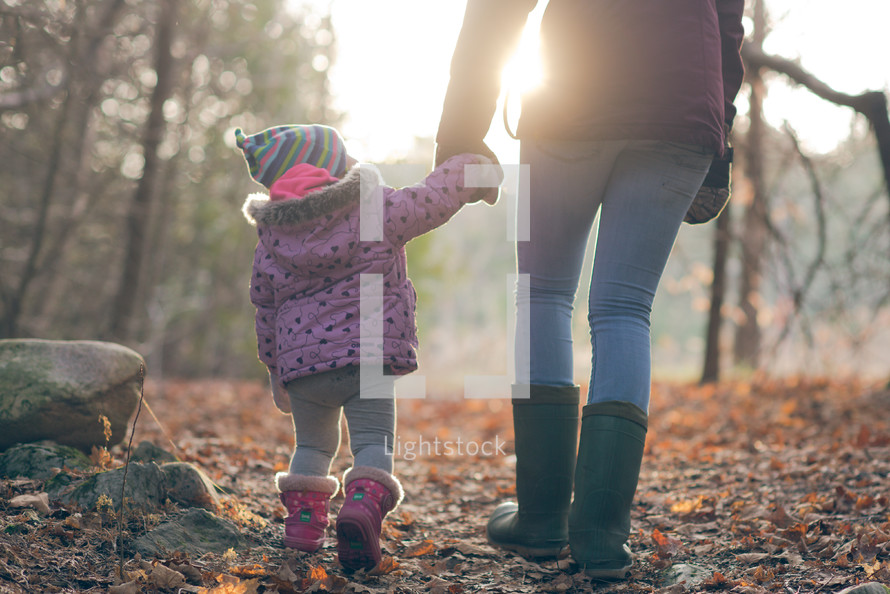 mother and toddler daughter walking in the woods in coats holding hands 