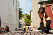 woman writing in a journal and iced coffee and cappuccino on a wooden table outdoors 