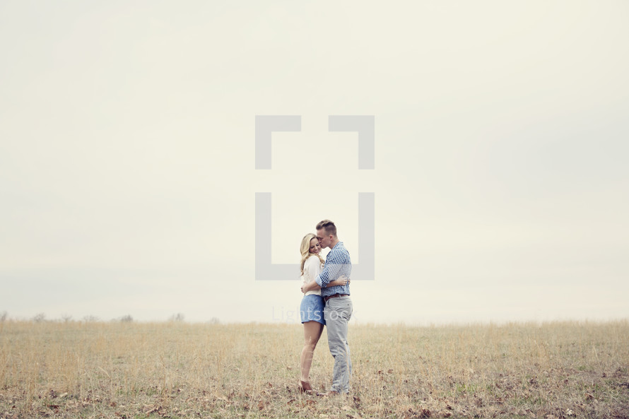 A man and woman embrace while standing in a field.