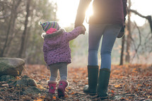 mother and toddler daughter walking in the woods in coats holding hands 