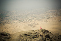 Person sitting atop a rocky mountain overlooking the desert.