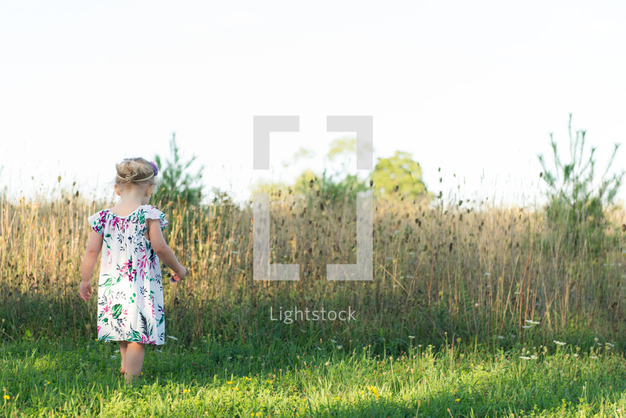toddler girl exploring a grass field 