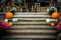 Beautiful autumn arrangement of pumpkins, flowers, gourds, wooden chairs, hay bales and tassels on wooden stairs.