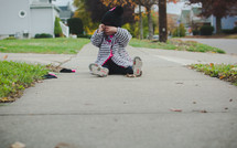 toddler girl in a sweater and wool cap sitting on a sidewalk 