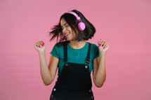 Attractive woman dancing with headphones on pink studio background. Cute girl portrait. Music, radio, happiness, freedom, youth concept