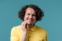 Handsome curly haired man with tooth pain on blue studio background. Toothache, dental problems, dentistry and medicine concept