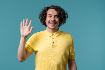 Friendly young man waving hand - hello, or goodbye, chao, salute. Parting, say bye to camera. Handsome man on blue studio background. High quality photo