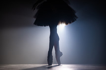 Close up silhouette of ballerina legs in tutu dress. Ballet performance on dark stage with floodlight backlight. Smoke background