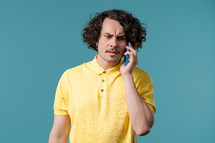 Annoyed young man quarreling while talking on mobile phone. Angry dude, stress. Blue studio background. Conflict, dispute, negative. High quality 