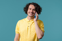 Smiling positive guy talking by phone, nice joke, smiling. Young man on blue background. Having smartphone call. High quality