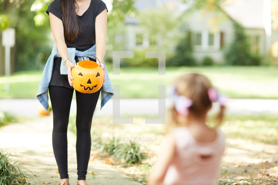 a woman holding a jack-o-lantern out for a child 