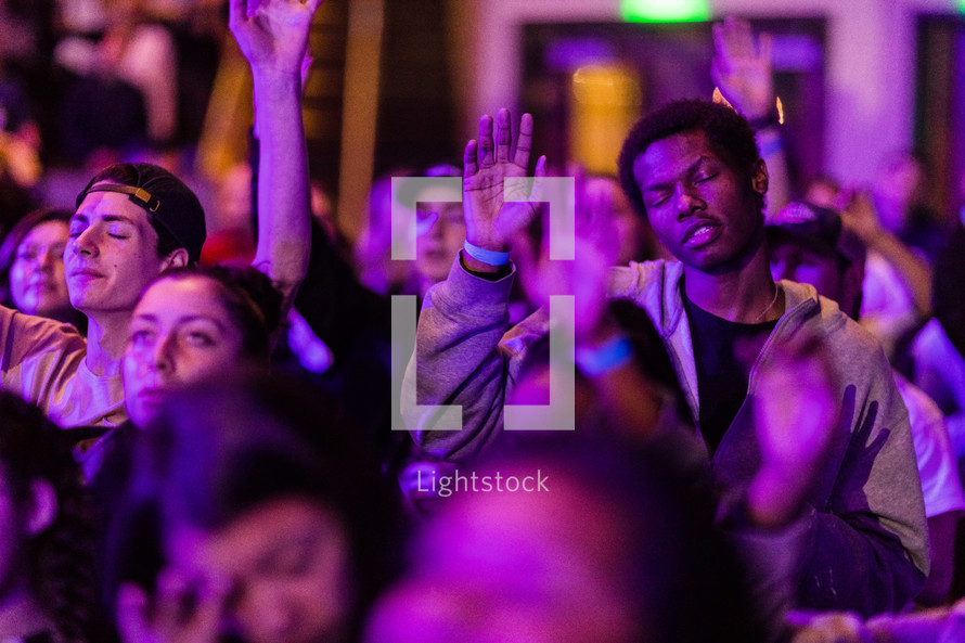 A group of people under purple light with their hands raised in praise and worship.