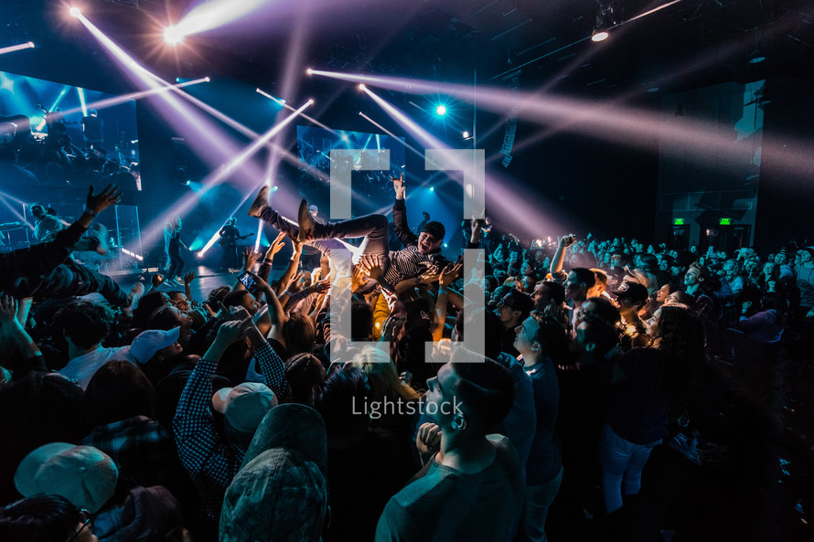 Stage lights on a large audience and a person being held up by others.