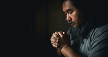 Man praying with folded hands in a dark room