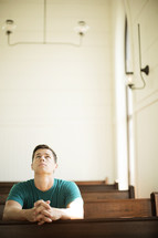 Man looking up while praying in a church pew.