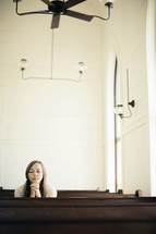 Woman praying in a church pew.