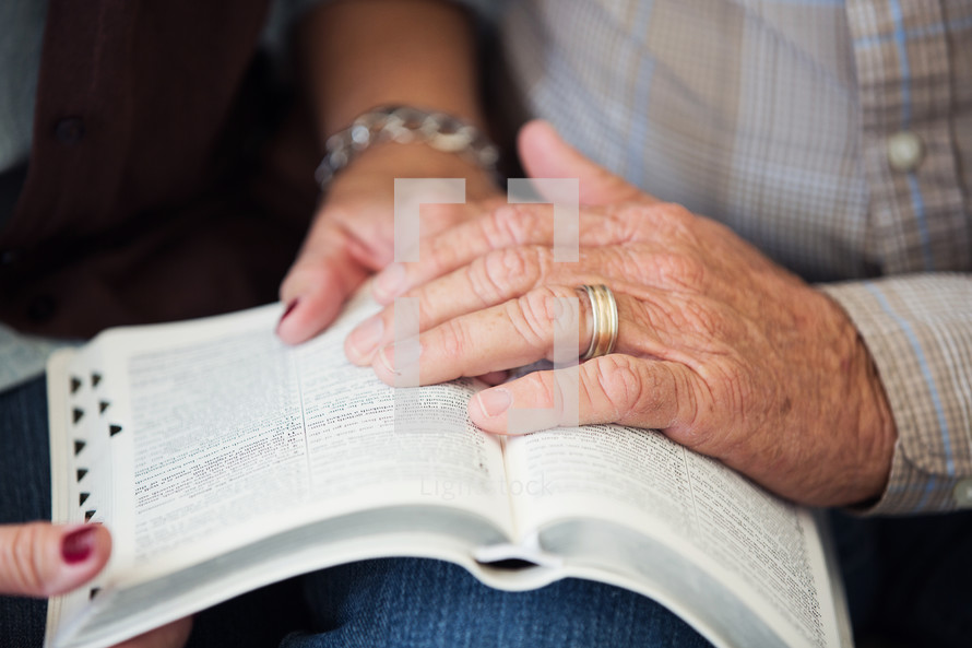 elderly couple praying over the pages of a Bible 