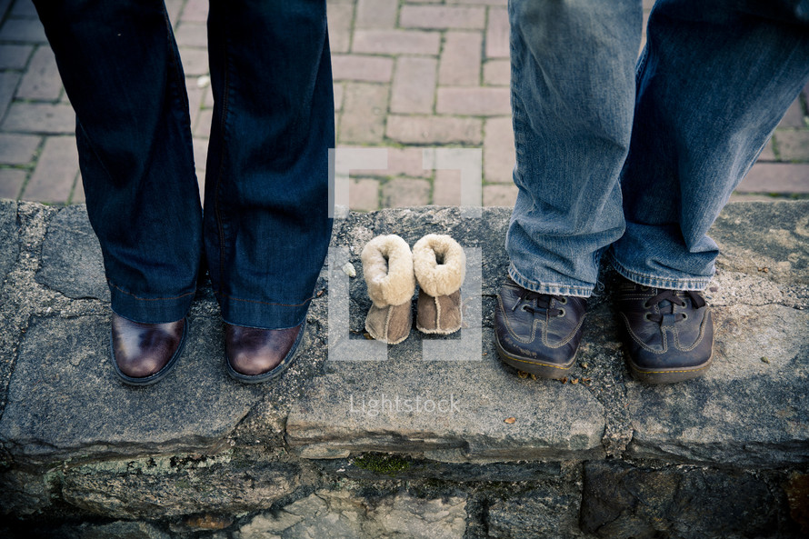 expectant parents standing beside empty baby shoes