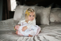 big sister holding her baby sister on a bed