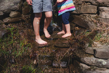 children standing on rocks in a stream 