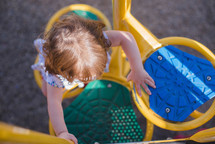 a toddler girl climbing up playground equipment 