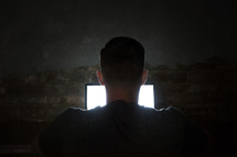 man looking at a computer screen in darkness.